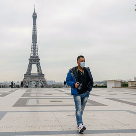 man wearing a face covering walks in Paris with the Eiffel Tower in the background